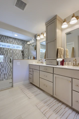 Modern double-sink bathroom with beige vanity, gold fixtures and glass shower, designed by ISM Construction.