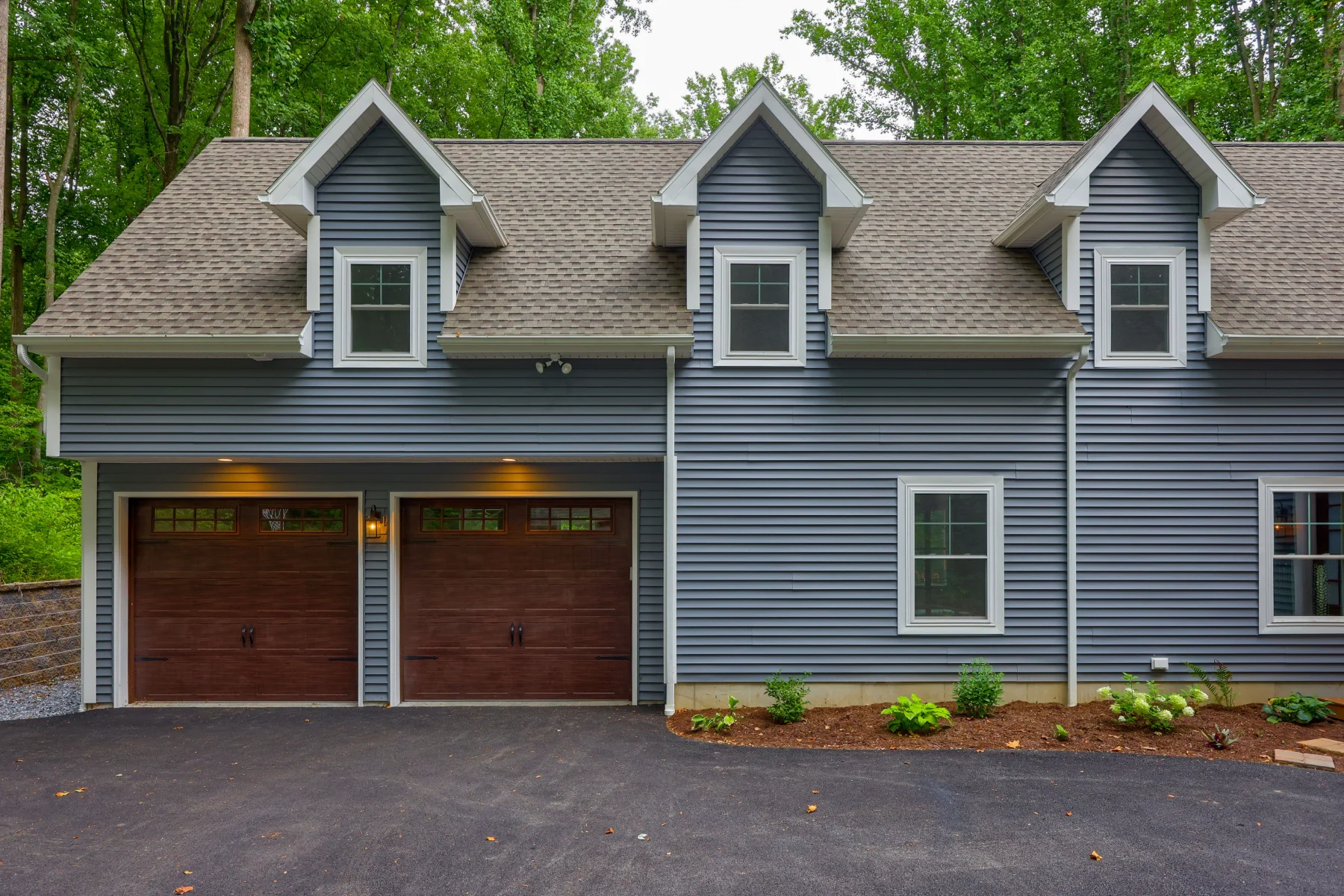 A blue house featuring two garages and a paved driveway in front.