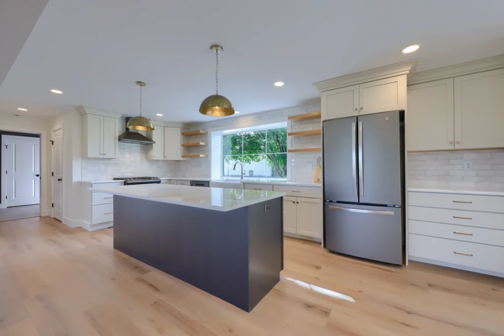 Contemporary kitchen with a dark island base, warm brass lighting, clean cabinetry lines and a bright window view styled by ISM Construction.